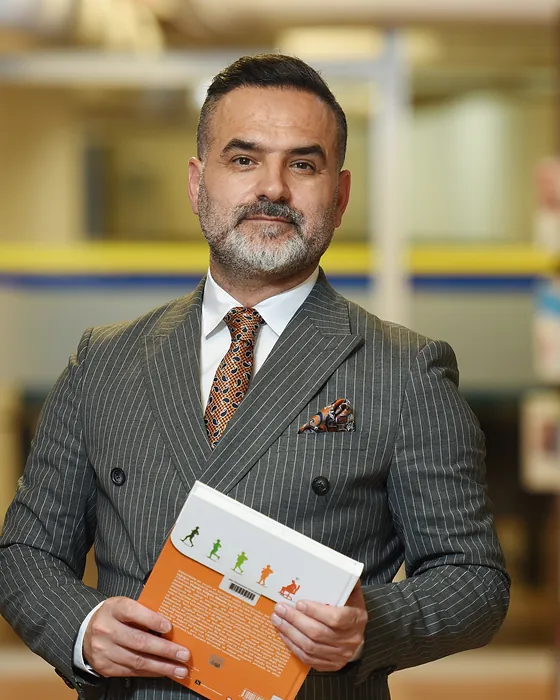 Aziz Aksöz, elinde bir kitapla ayakta